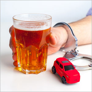 A hand, with handcuffs, holds a glass of beer and red toy car sits next to the glass | Sexton Weldon Law Firm