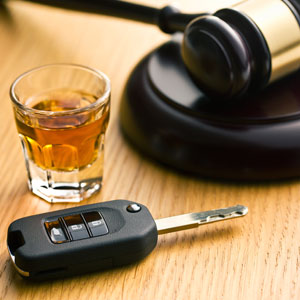 A glass filled with liquid sits on a wooden table, next to a car key and a gavel | Sexton Weldon Law Firm