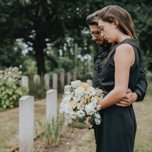 A couple in a black dress embraces tenderly in a serene cemetery, surrounded by gravestones | Sexton Weldon Law Firm