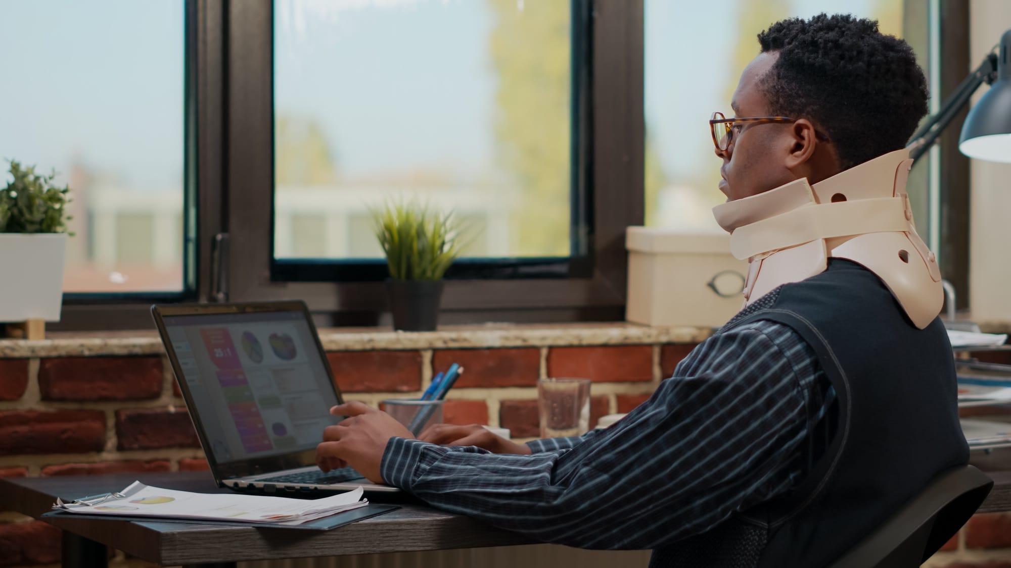 Injured worker with cervical collar using laptop to plan finance